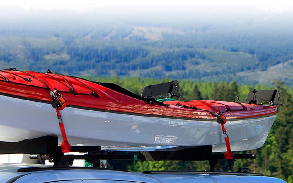 orange and white kayak secured by orange Strapinno retractable tie-downs on top of a vehicle