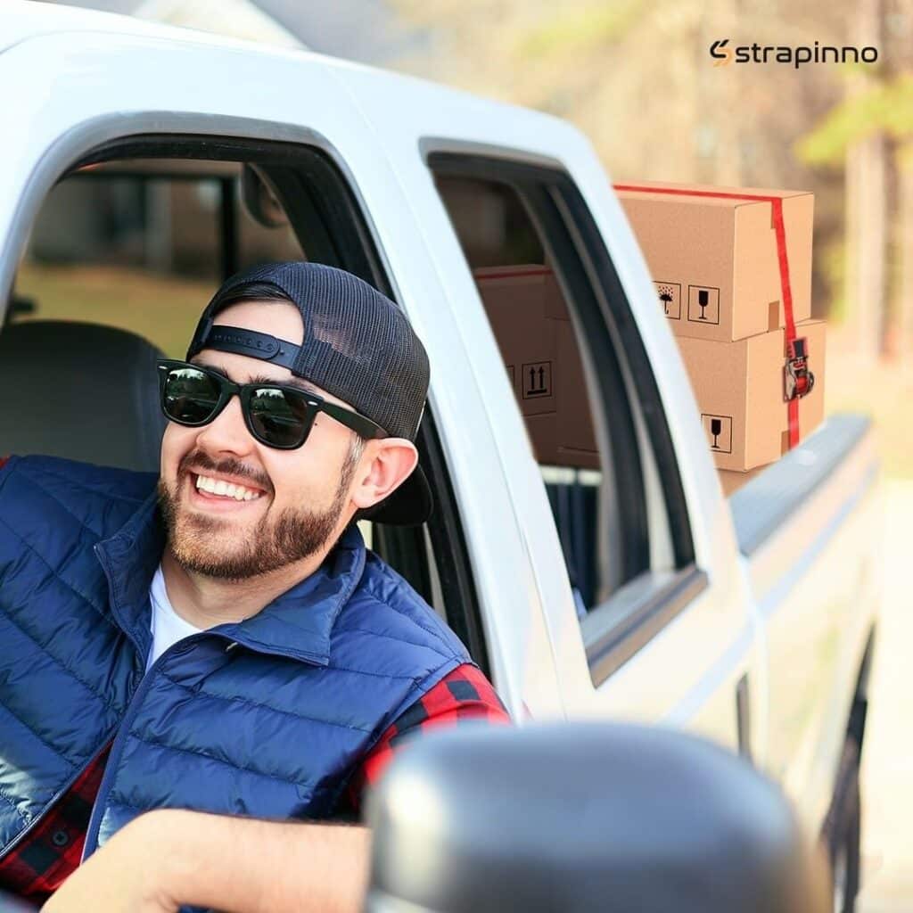 smiling man with sunglasses and cap inside pickup truck with cargo secured by Strapinno retractable ratchet straps