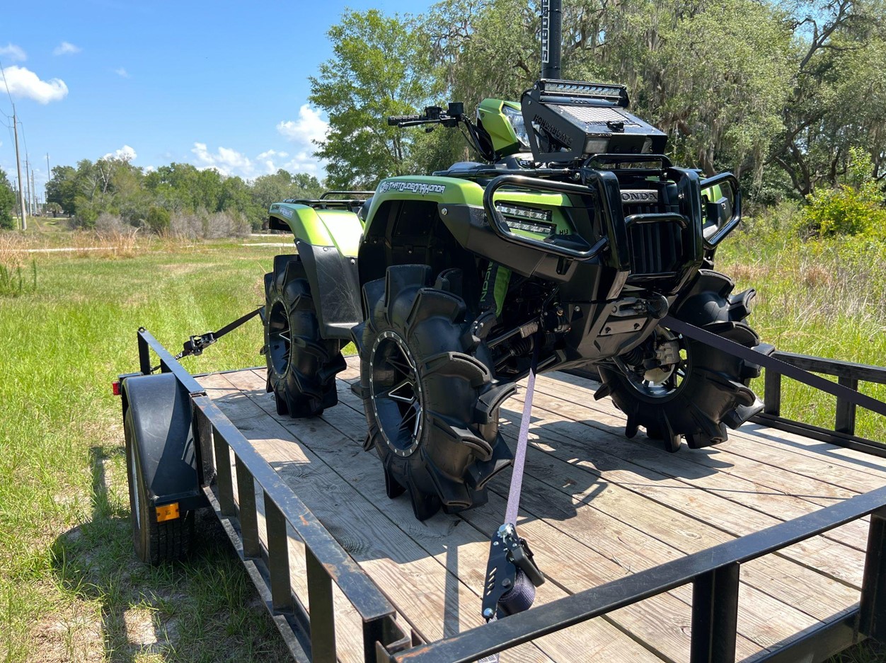 atv with black and lime green colors secured with Strapinno retractable ratchet straps on wooden trailer bed
