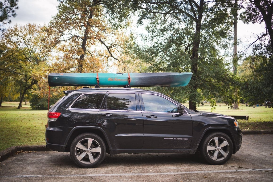 teal kayak secured on top of black sedan using retractable ratchet straps from Strapinno