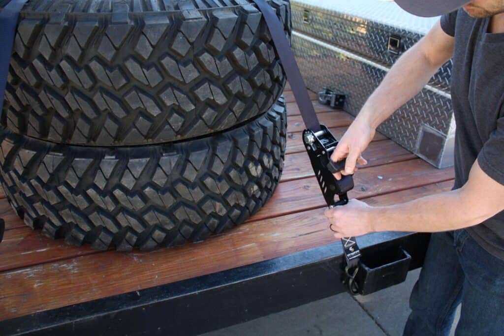 person securing large tires on a truck bed using Strapinno retractable tie-down straps