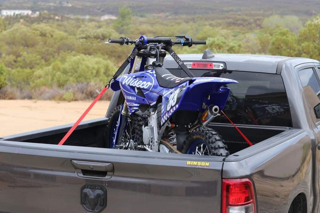 blue motorcycle secured on a gray pickup truck trailer using Strapinno's retractable ratchet staps