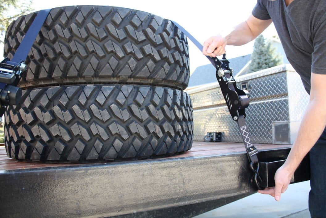 person securing two large tires using Strapinno's black retractable ratchet straps
