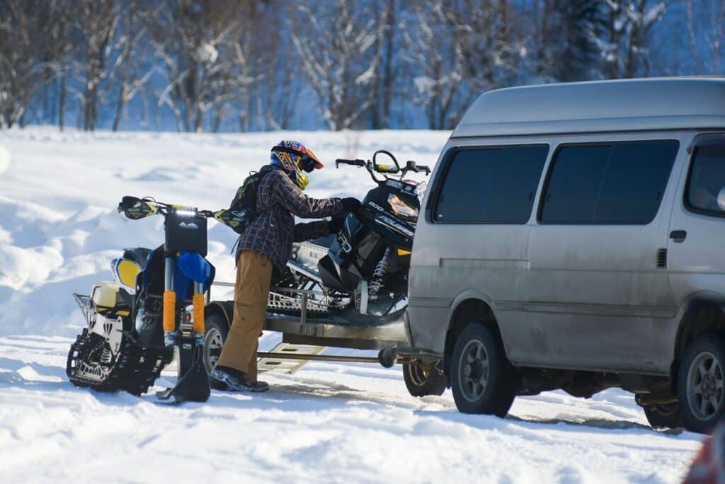 person wearing a helmet loading a snowmobile onto a trailer at the back of a van