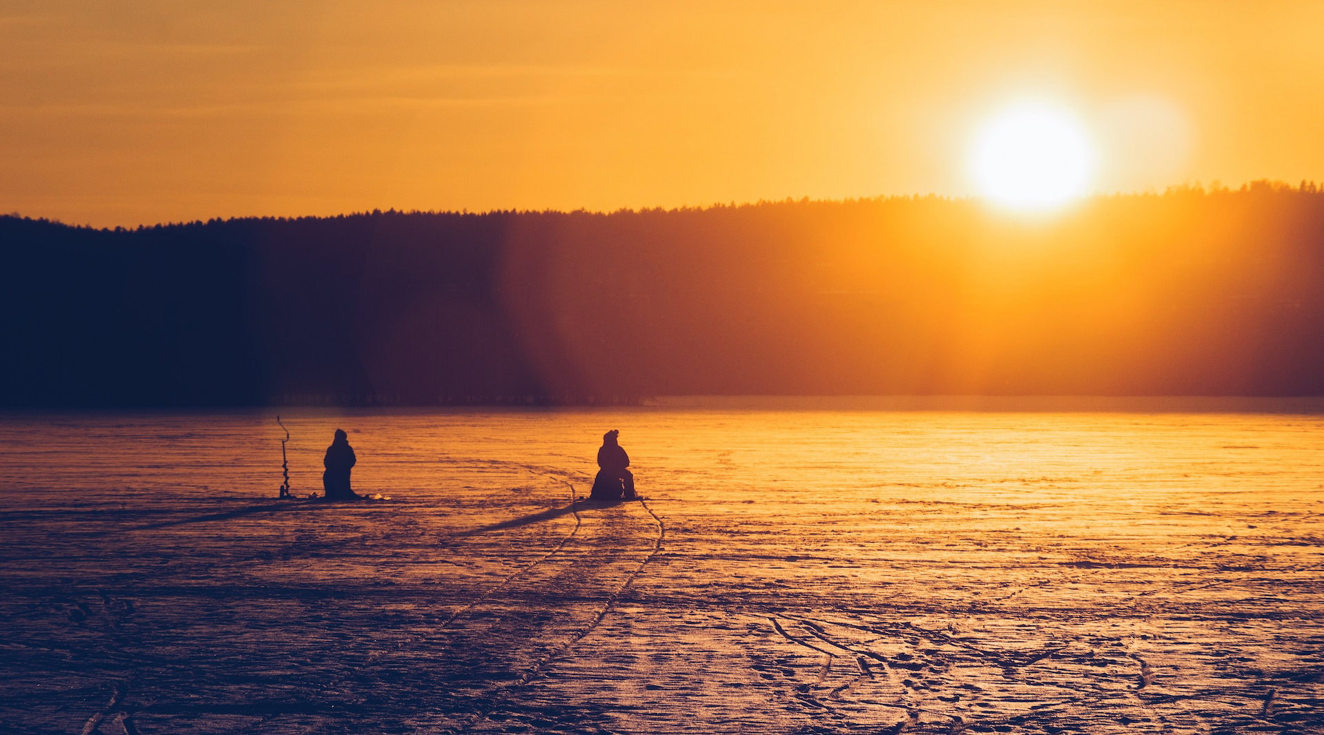 silhouette of two people ice fishing in the sunset