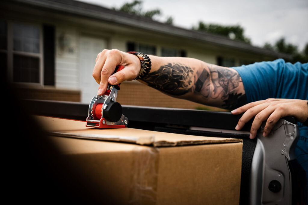 tattooed arm of man securing a box on a pick up truck using Strapinno's retractable tie-down straps