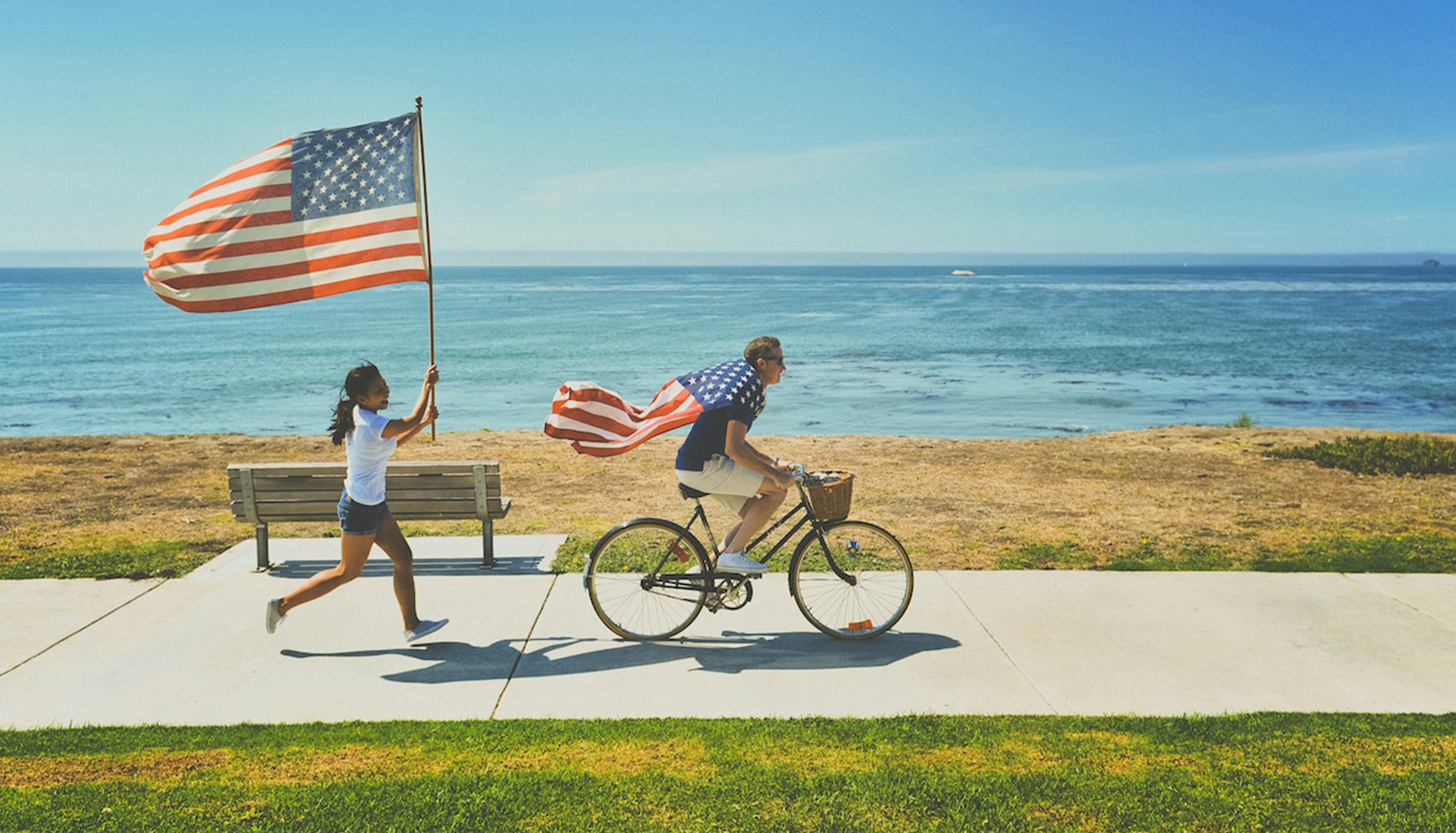 a woman running with the US flag following a guy on a bike with the beach in the background