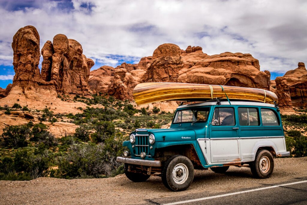 teal and white SUV with wooden canoe on roof secured by retractable ratchet straps