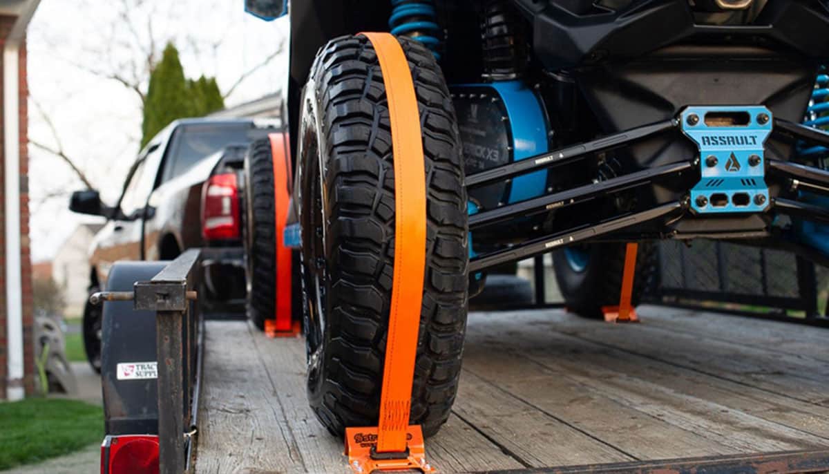 close up shot of an ATV's wheel secured by Strapinno's orange retractable ratchet straps with wheel chocks on a trailer